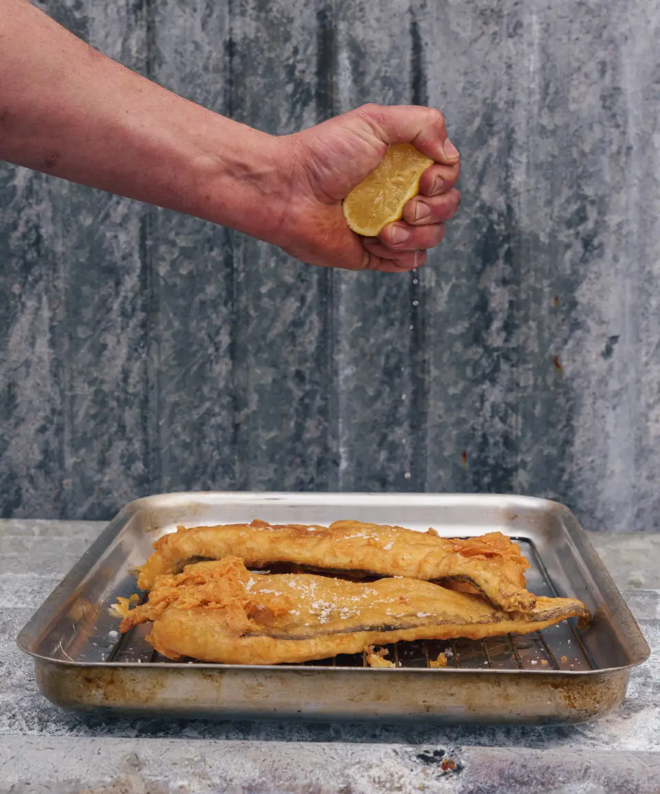 Chef squeezing lemon on fish and chips at Proper Kitchen