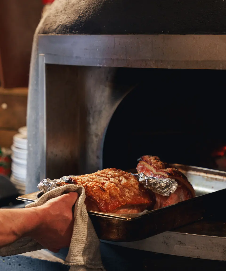 Chef putting roast joint of meat in wood fired oven at Proper Kitchen